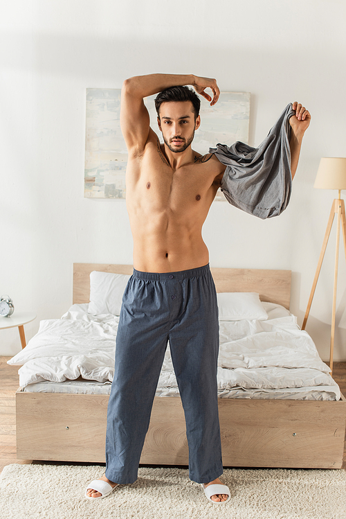 Bearded man taking off t-shirt in bedroom