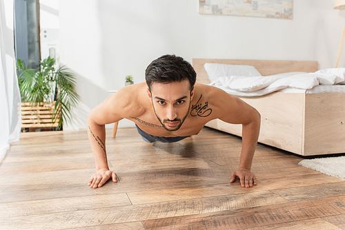 Shirtless man doing press ups in bedroom in morning