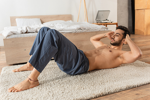 Shirtless man doing abs while working out on carpet in bedroom