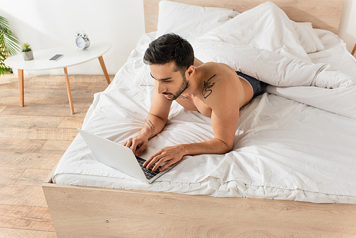 Overhead view of tattooed man using laptop on bed in morning