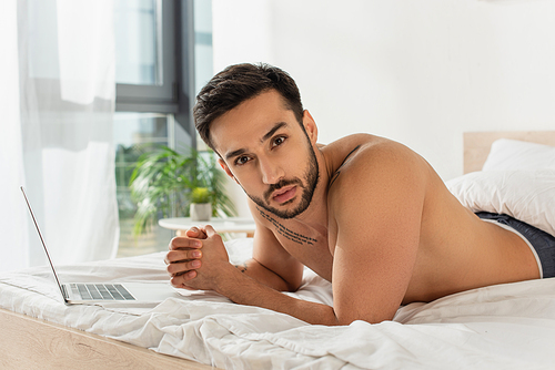 Shirtless man  near laptop on bed at home
