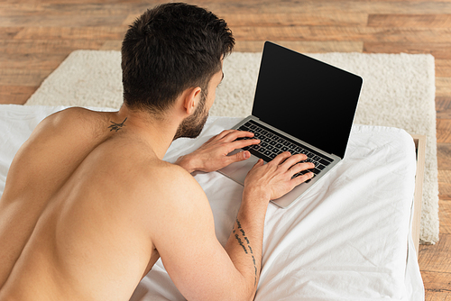 Overhead view of shirtless man using laptop with blank screen on bed