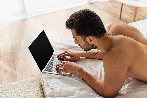 High angle view of shirtless teleworker using laptop with blank screen on bed