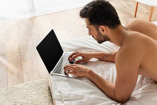 High angle view of tattooed man using laptop with blank screen on bed