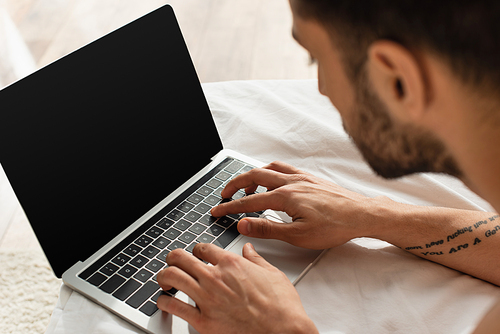 Blurred man using laptop with blank screen on white bedding