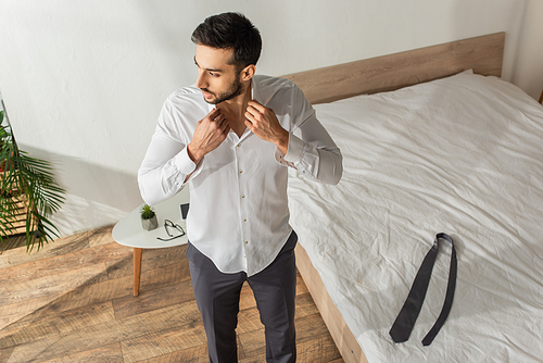 Overhead view of businessman wearing shirt near tie on bed in bedroom at home