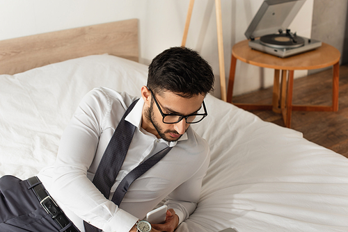 Businessman in eyeglasses holding cellphone on bed