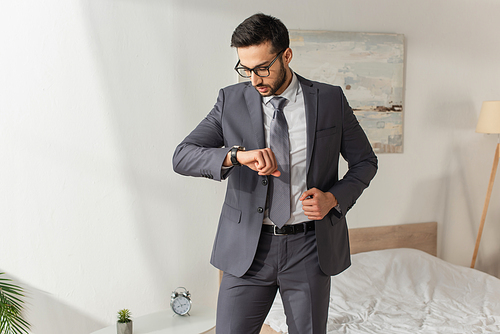 Businessman in eyeglasses looking at wristwatch in bedroom