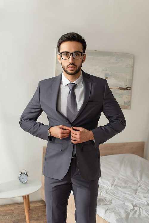 Bearded businessman buttoning jacket in bedroom at home