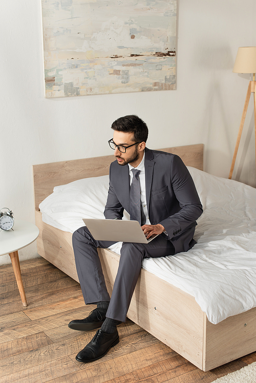 Young businessman using laptop while sitting on bed
