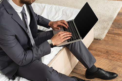 Cropped view of businessman in suit using laptop with blank screen on bed