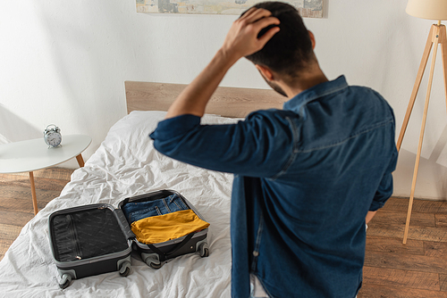 Back view of blurred man looking at suitcase on bed