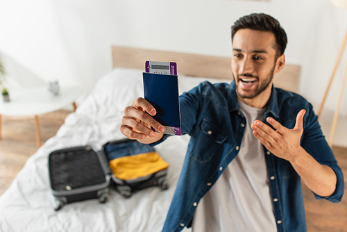Blurred man pointing at passport with air ticket near suitcase on bed
