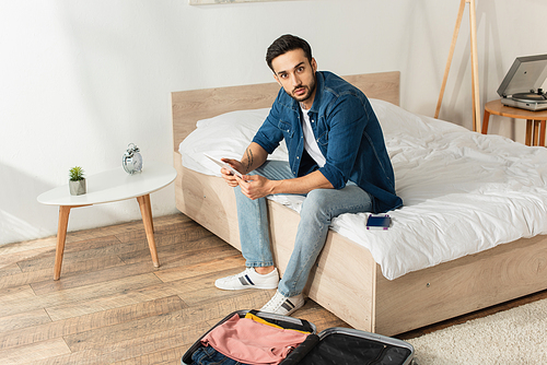 Young traveler with digital tablet  near suitcase and passport in bedroom