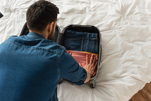 Overhead view of man putting cloths in baggage on bed