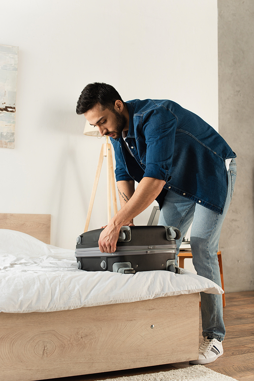 Bearded traveler fastening suitcase on bed at home