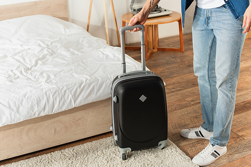 Cropped view of traveler holding suitcase in bedroom