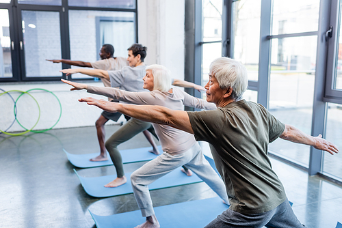Elderly asian man practicing yoga near multiethnic people in sports center