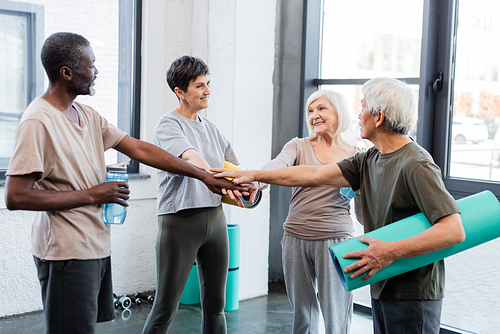 Elderly interracial people holding fitness mats and hands in gym