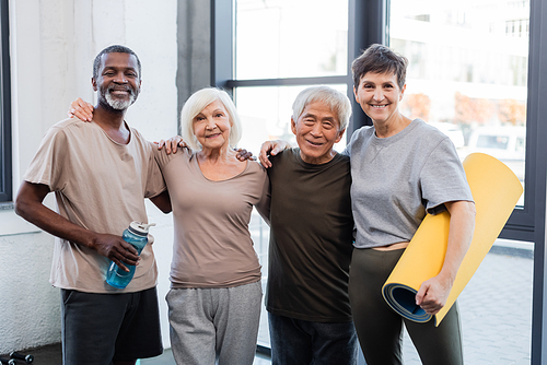 Senior multiethnic people hugging and smiling at camera in gym