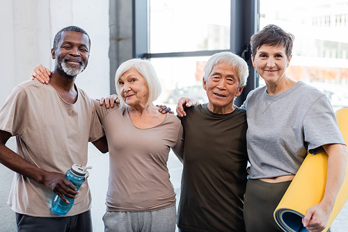 Elderly multiethnic people in sportswear hugging in gym