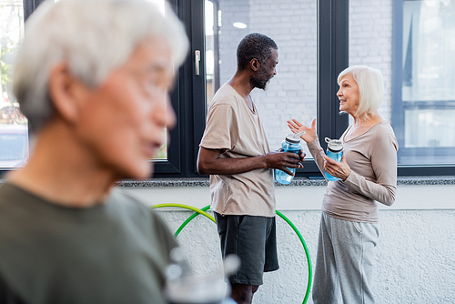 Gray haired woman with sports bottle talking to african american man in sports center