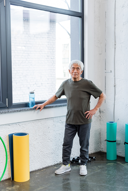 Elderly asian man  near fitness mats and sports bottle in gym