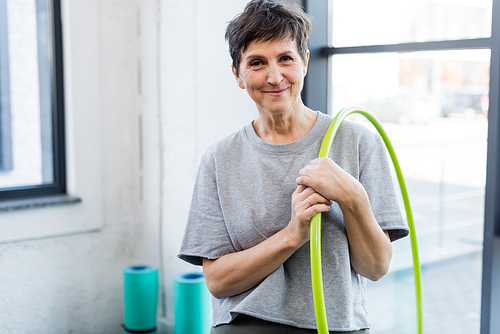 Smiling senior woman holding hula hoop in sports center