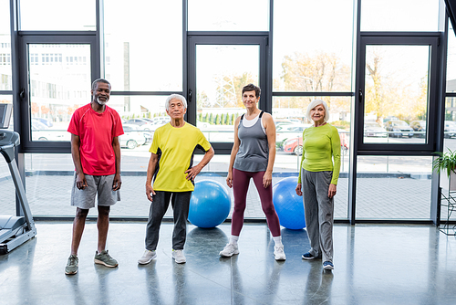 Positive multiethnic senior people  near fitness balls and treadmill in gym