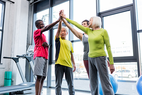 Cheerful interracial senior people giving high five in sports center