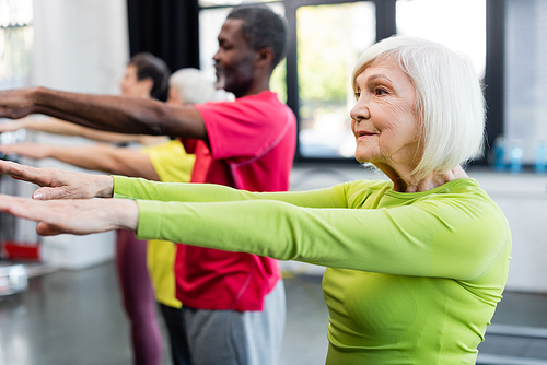 Elderly sportswoman training near blurred multiethnic people in sports center