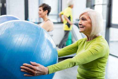 Grey haired sportswoman training with fitness ball in sports center
