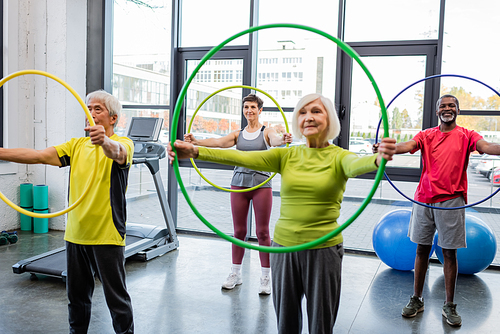 Interracial elderly people training with hula hoops in sports center