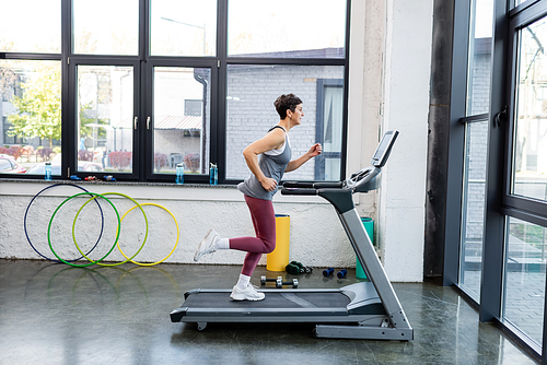 Side view of sportswoman training on treadmill in sports center