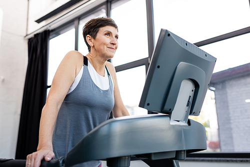 Smiling sportswoman working out on treadmill in gym