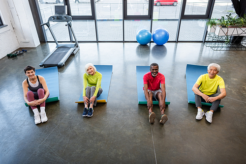 High angle view of multiethnic senior people sitting on fitness mats in gym