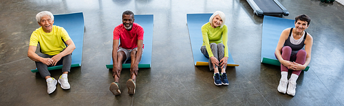 High angle view of smiling interracial senior people  on fitness mats in gym, banner