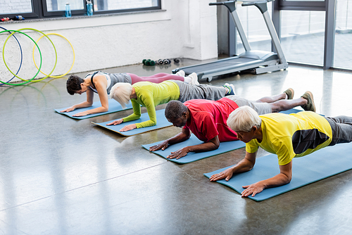 Elderly multiethnic people standing in plank on fitness mats
