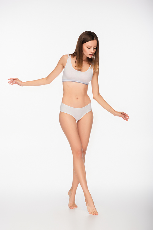 full length view of young woman with slim body walking on tiptoes on white background
