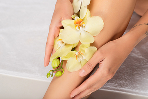 cropped view of woman with orchid on smooth leg sitting on white towel