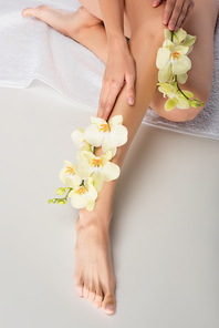 cropped view of barefoot woman with smooth skin sitting on white towel with orchids