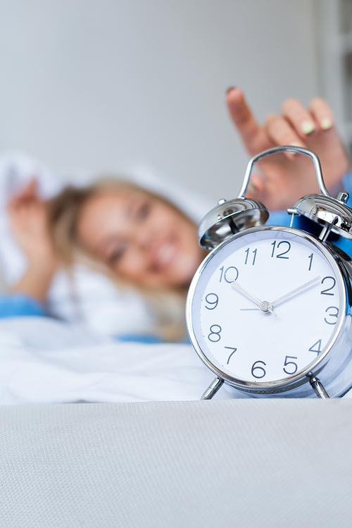 happy and blurred woman reaching retro alarm clock