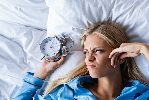 top view of displeased woman holding retro alarm clock