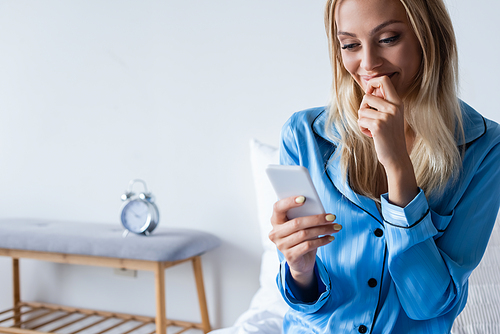 happy woman in pajamas talking on smartphone in bedroom