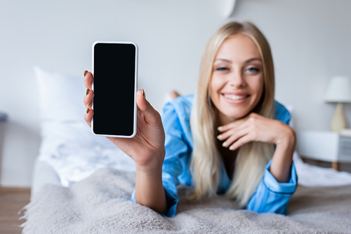 blurred and happy woman in pajamas holding smartphone with blank screen in bedroom