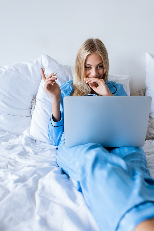 joyful young woman in pajamas watching comedy movie on laptop in bedroom