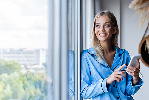 happy young woman holding cellphone and looking at window