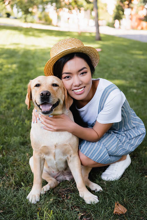young asian woman smiling at camera while hugging dog in park