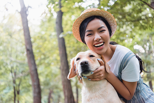 excited asian woman smiling at camera while hugging dog outdoors