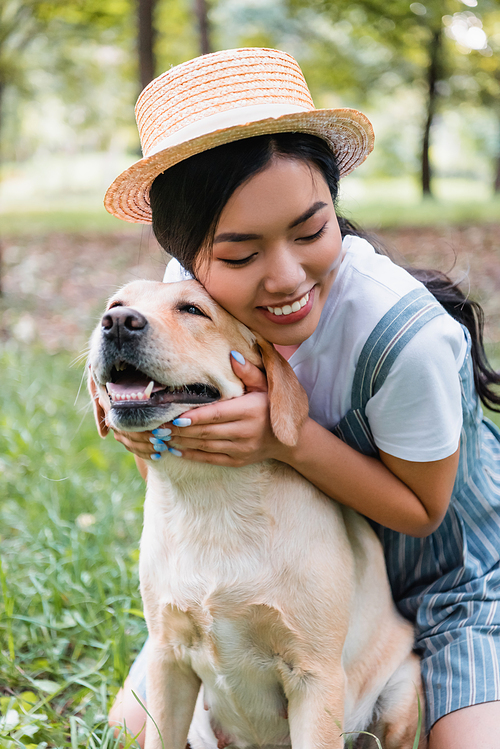 young and happy asian woman cuddling yellow labrador in park